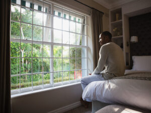 Man sitting on bed by window looking out at trees